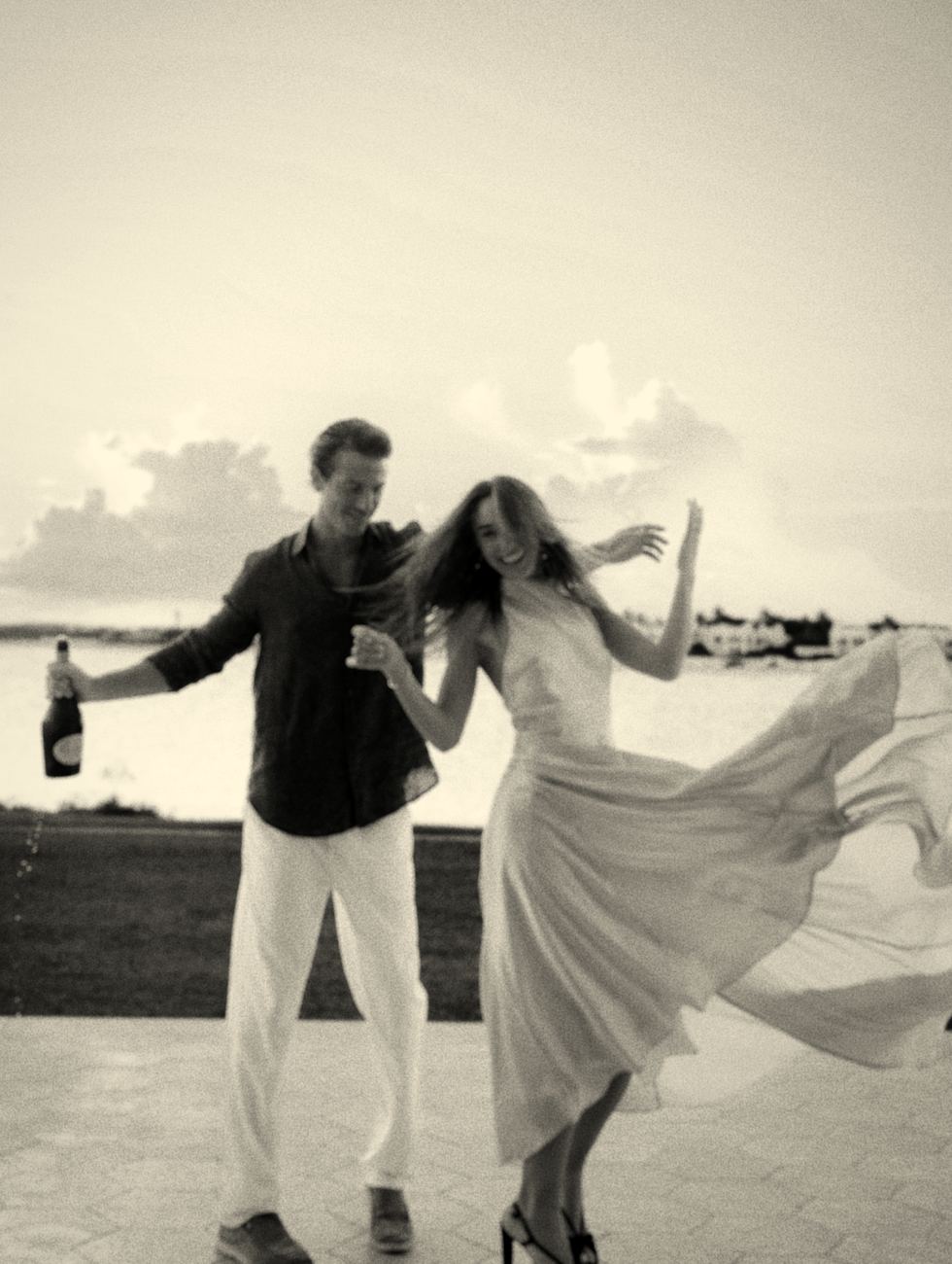 Mari twirling her dress beside Graftan holding champagne